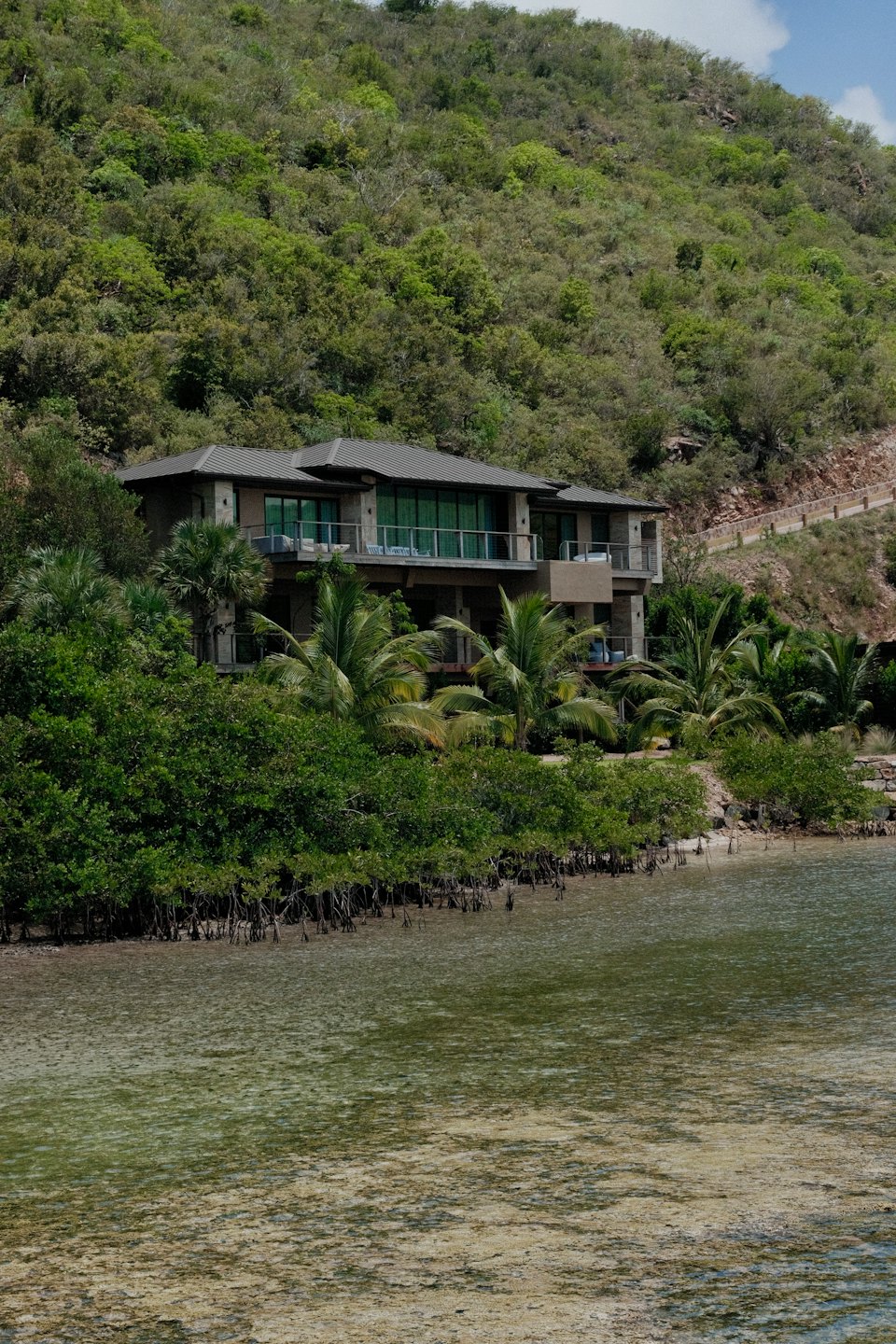 Modernes Haus mit Glasfenstern an einem grünen Hang mit Blick aufs Wasser.
